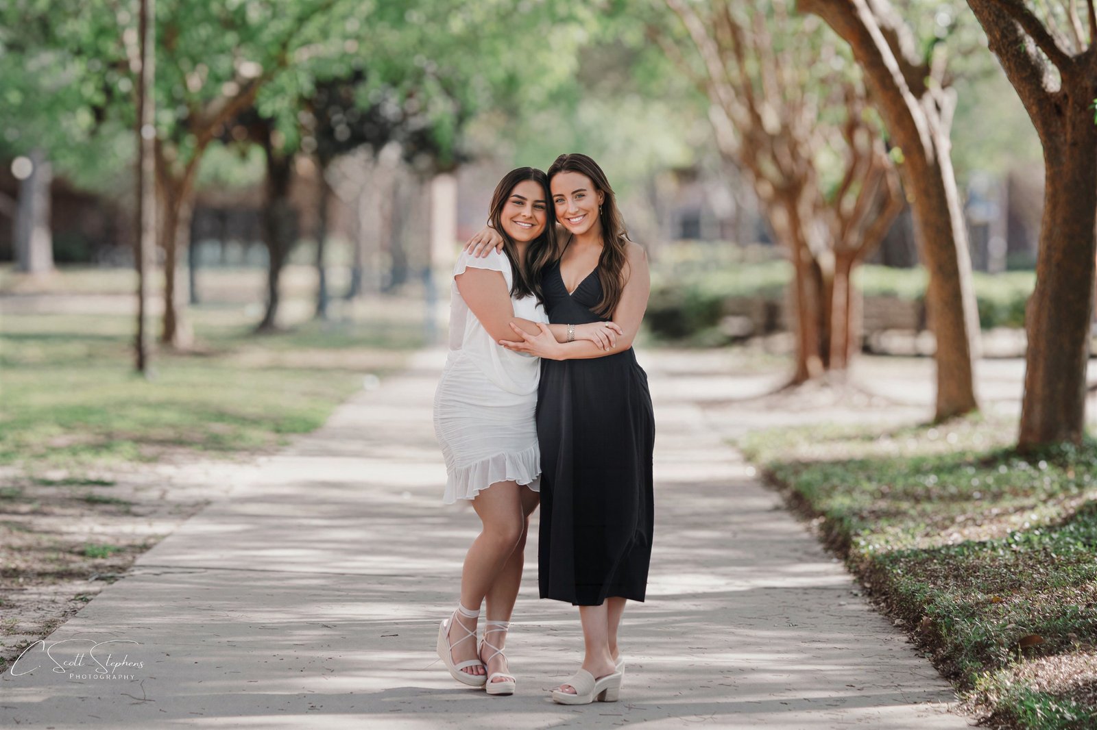 Two women embracing on a tree-lined walkway